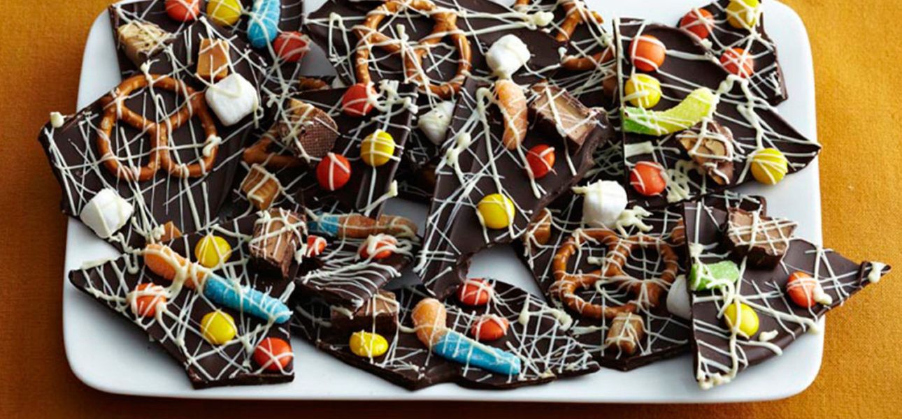 Smashed chocolate bark covered in candy such as mini-pretzels, gummy worms, marshmallows, M&Ms, and icing.