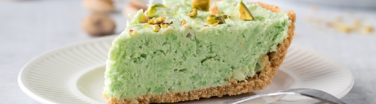 Slice of pistachio cheesecake on a white plate with pistachios in background